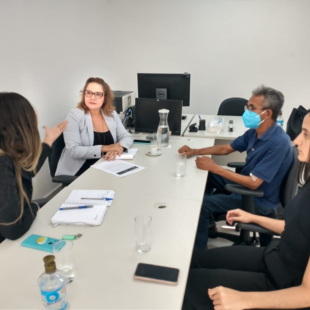 Imagem de uma reunião com três mulheres e um homem, sentados à mesa.