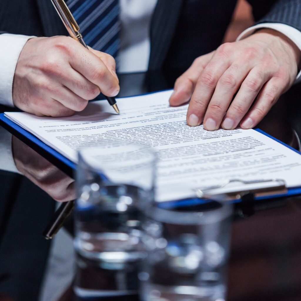 imagem de um homem, sem aparecer o rosto, assinando um documento.