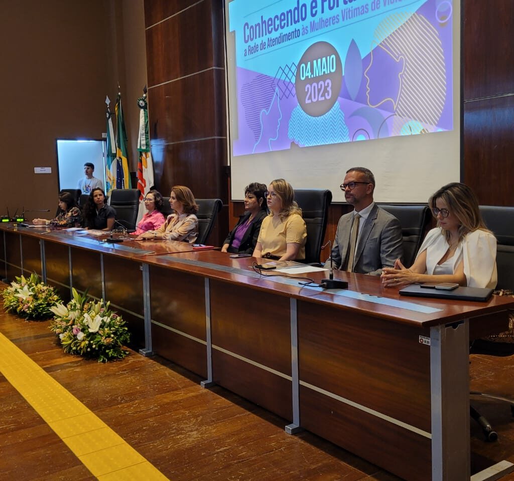 Imagem com várias pessoas sentadas à mesa, em um auditório