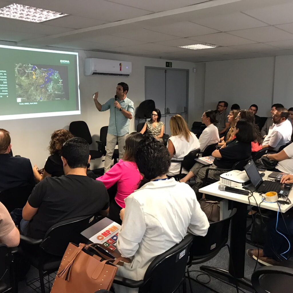 Imagem de um mini-auditório com várias pessoas sentadas, assistindo a uma palestra.