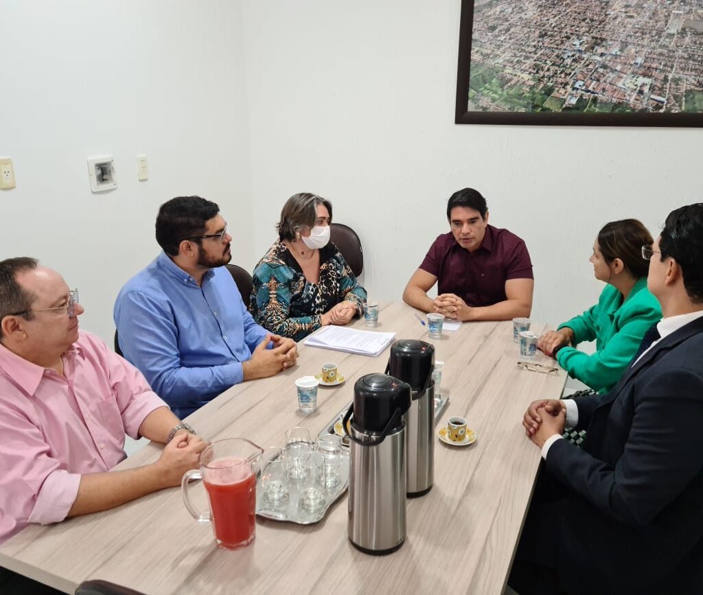 Imagem com várias pessoas sentadas ao redor de uma mesa, conversando.