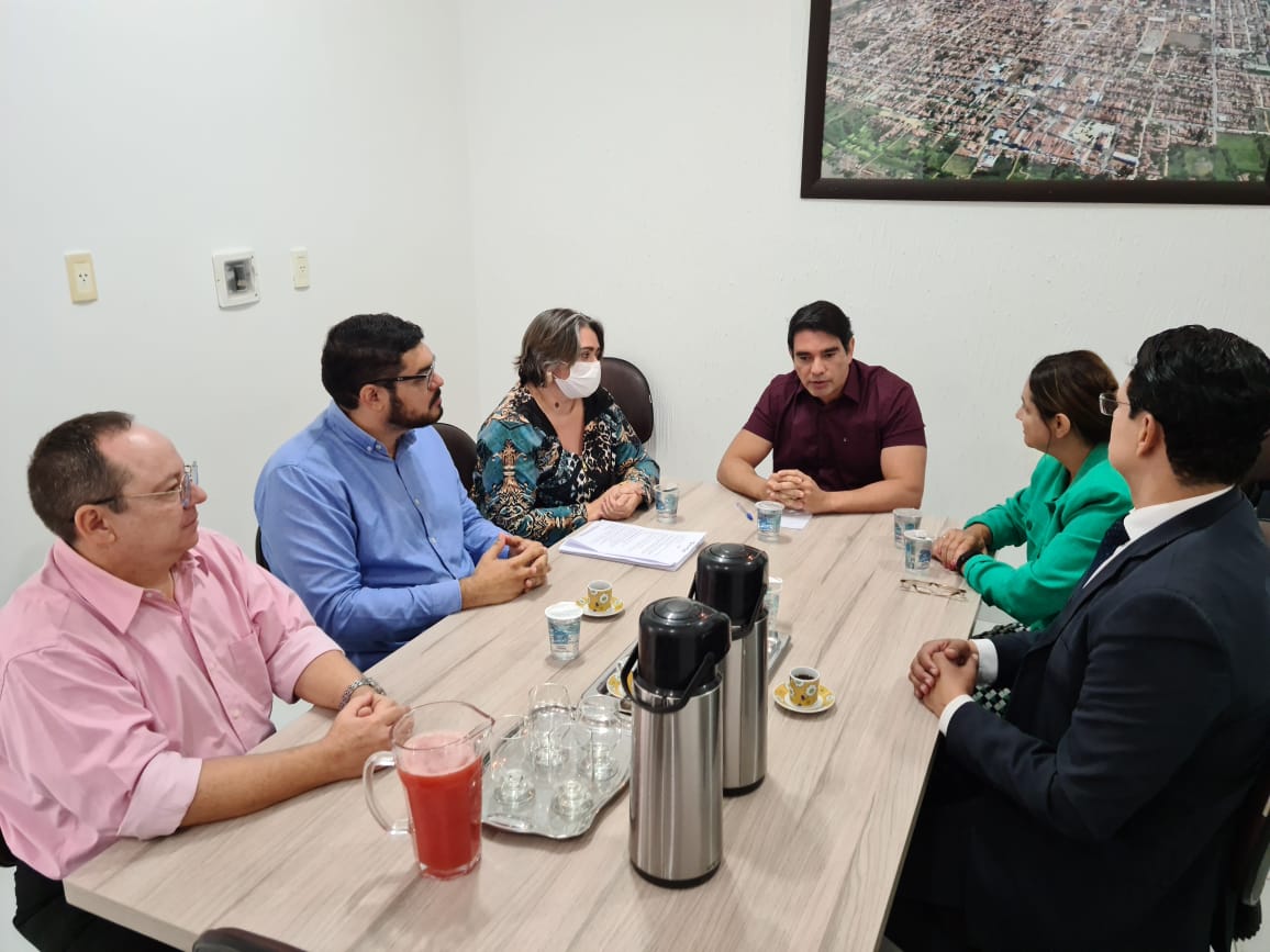 Imagem com várias pessoas sentadas ao redor de uma mesa, conversando.