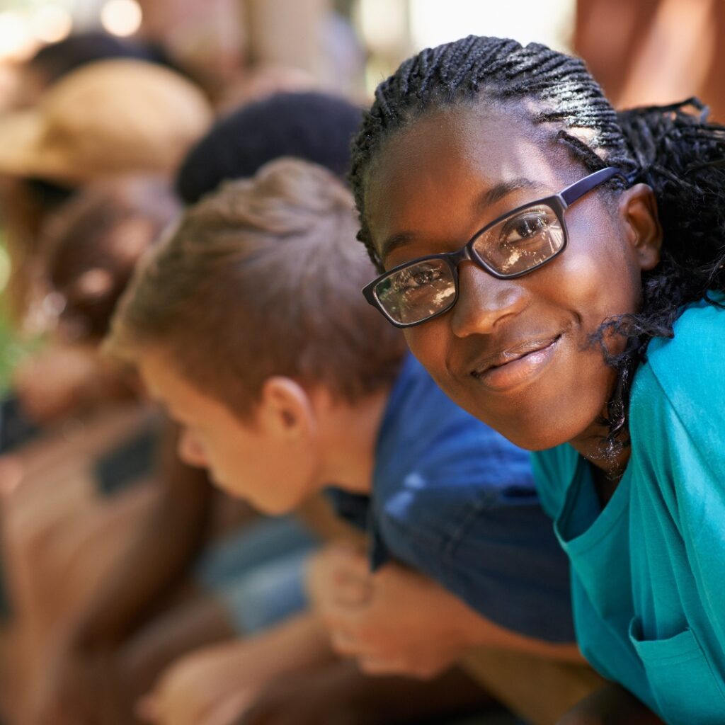 Imagem de uma adolescente negra, sorrindo, em primeiro plano, e crianças em segundo plano.