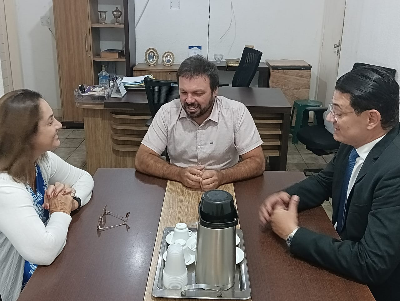 Imagem de dois homens e uma mulher, sentados ao redor de uma mesa, conversando.