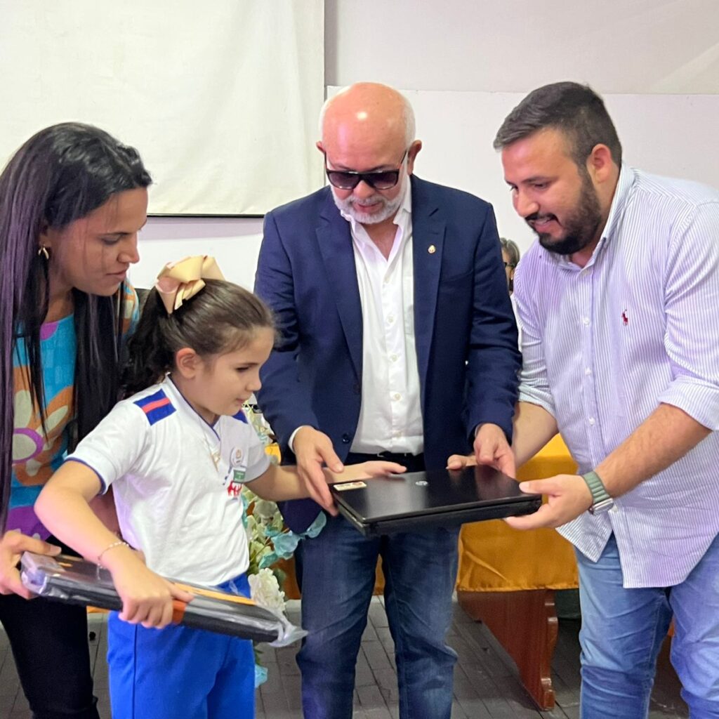 Imagem com quatro pessoas, sendo uma mulher, dois homens e uma de criança, esta última recebendo notebook das mãos dos dois homens.