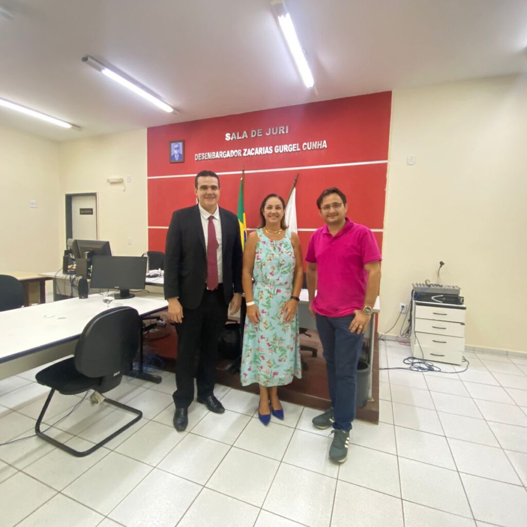 Imagem de três pessoas, sendo dois homens e uma mulher, em pé, posando para uma foto, em uma sala.