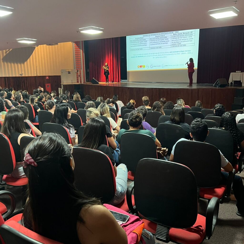 Imagem de um auditório repleto de pessoas assistindo a uma palestra.