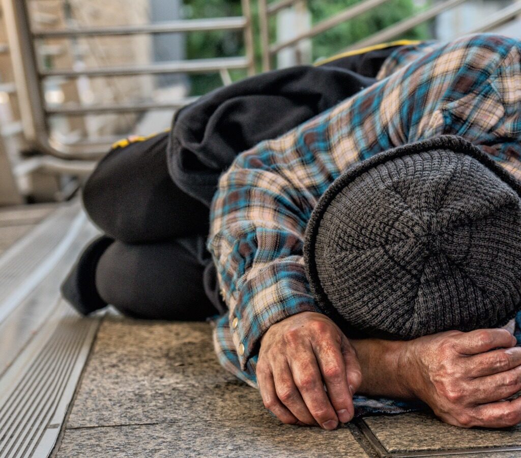 Imagem de um homem em situação de rua, dormindo em uma calçada.