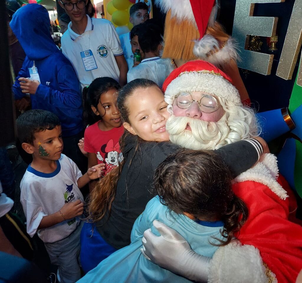 Imagem de papai noel sorrindo abraçando duas crianças.