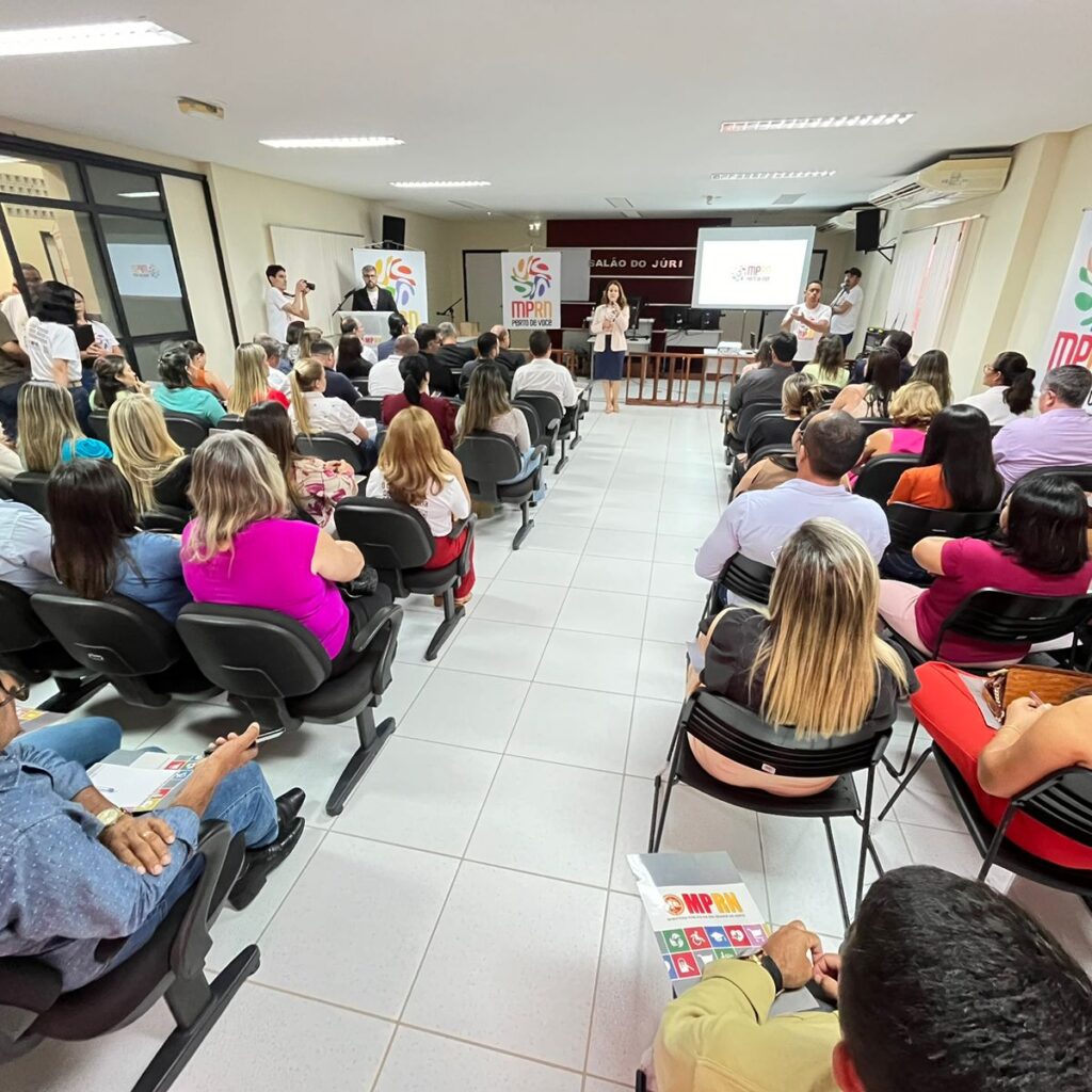 Imagem de várias pessoas sentadas, em um auditório, na abertura do MPRN Perto de Você, na cidade de Santo Antônio, ouvindo a procuradora-geral de Justiça Elaine Cardoso falar ao microfone.