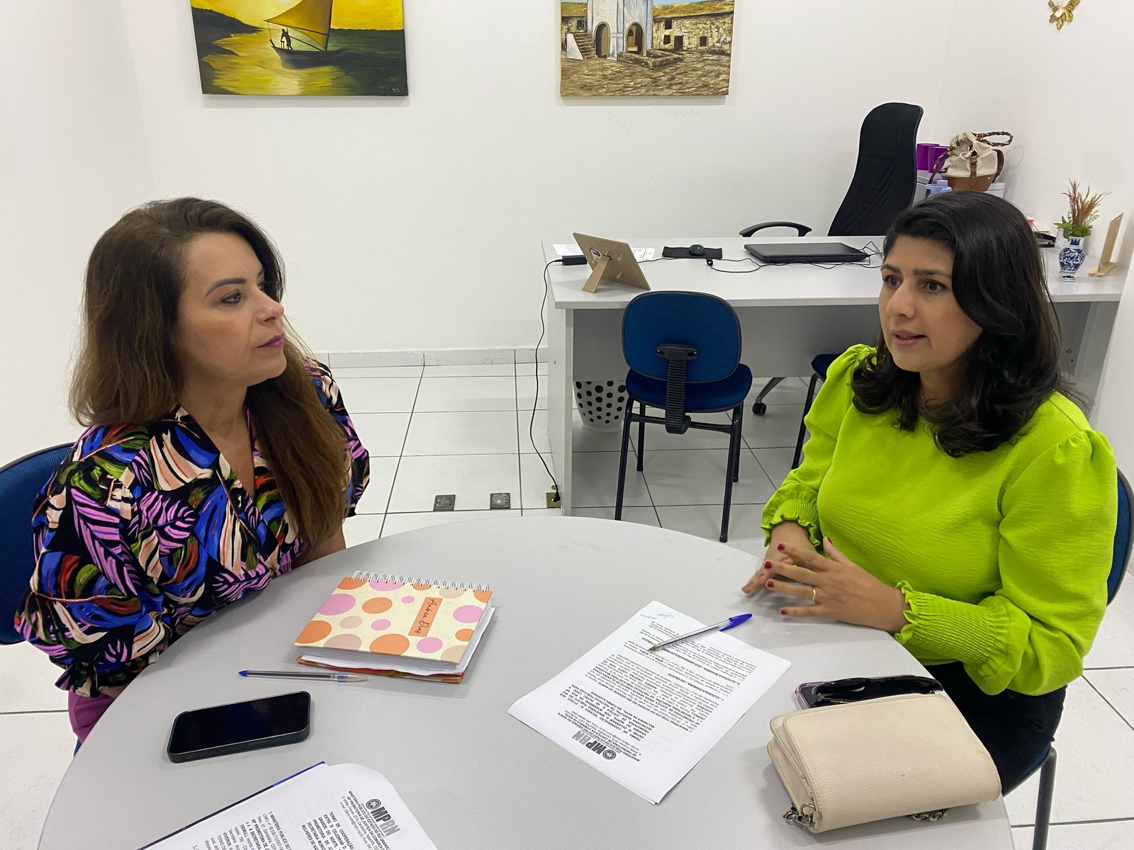 Imagem mostra a promotora e a Secretaria de Defesa da Mulher em Natal sentadas em uma mesa conversando