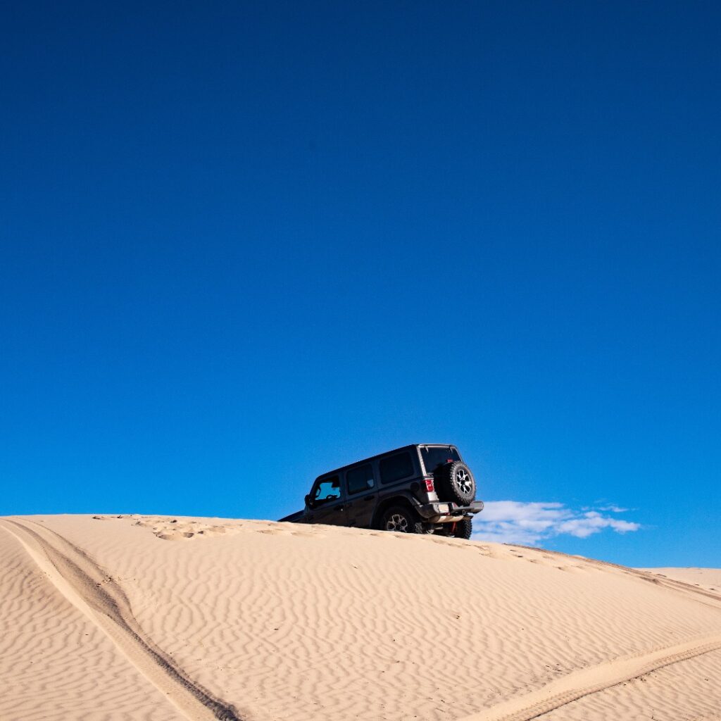 imagem de duna com marcas de pneus e um carro praticando off-road