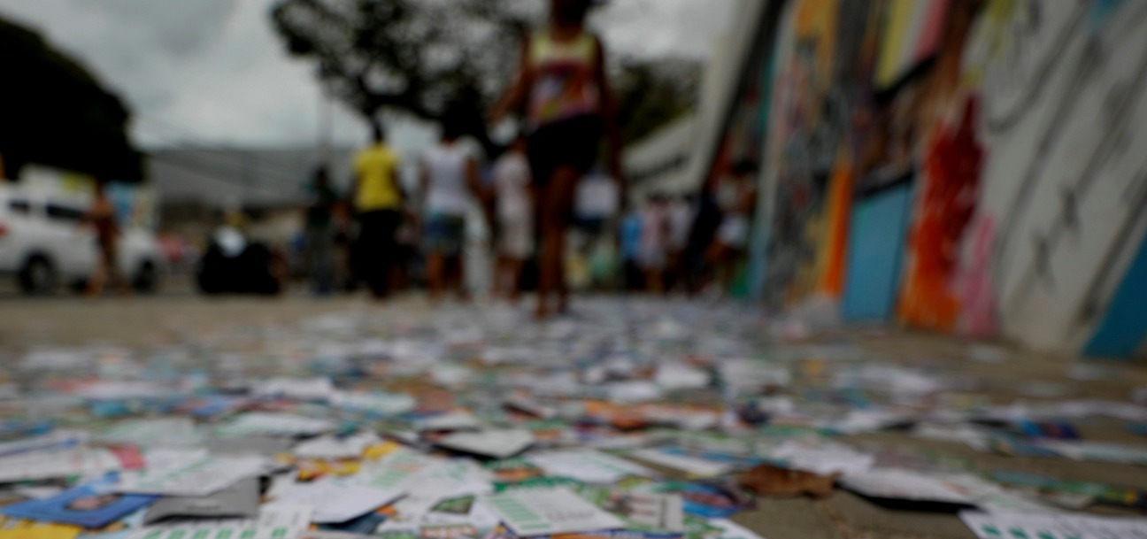 rua urbana com o chão completamente coberto por santinhos e panfletos de campanha eleitoral.